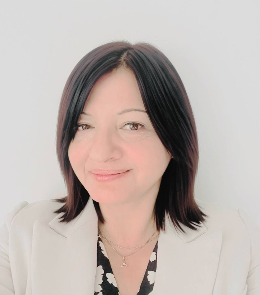 Dr Mihaela Bucur, consultant psychiatrist, smiling gently, with shoulder-length dark hair, wearing a light blazer over a patterned top.